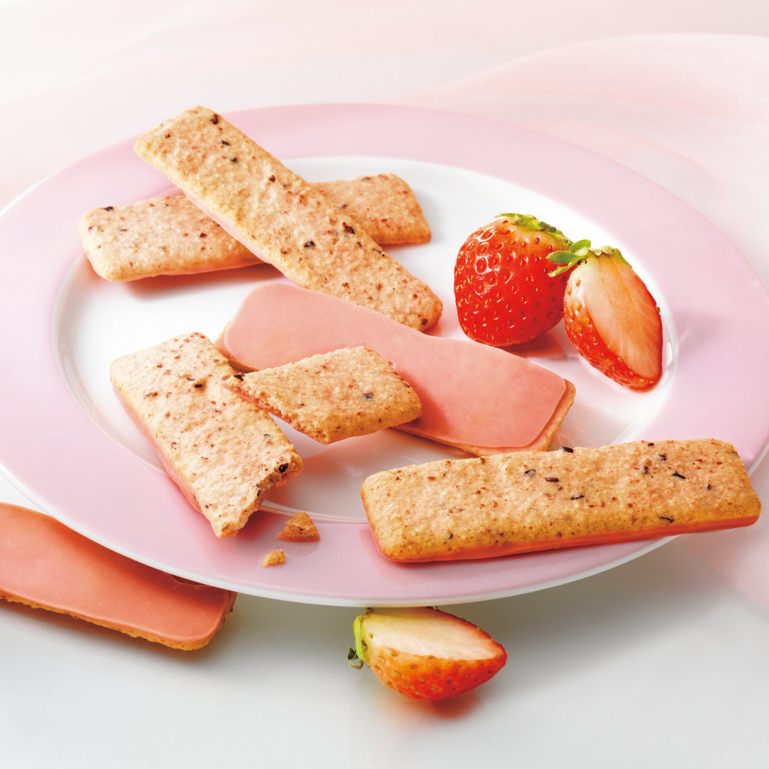 A pink plate holding several rectangular golden-baked cookies with cacao nibs, arranged with slices of strawberries on a light background.