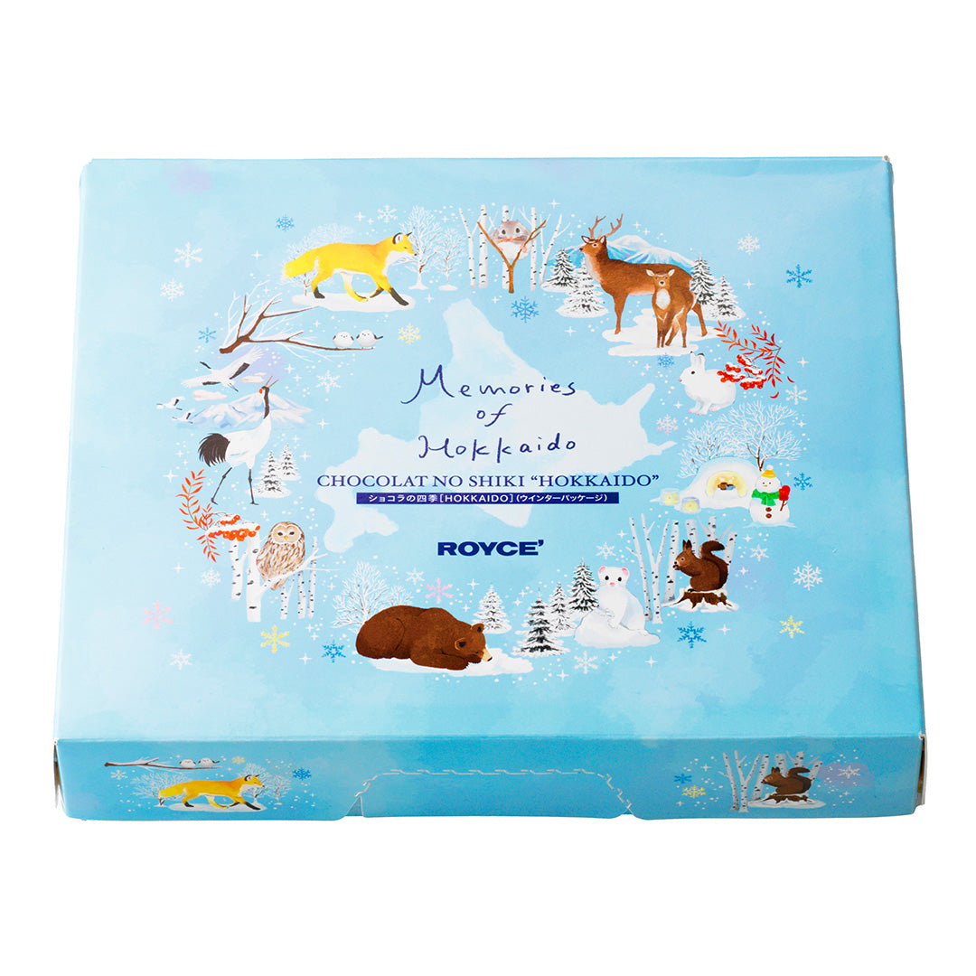 Image shows a blue box with illustrations of foxes, deer, a crane, owls, a bear, squirrels, a snowman, a cat, a rabbit, and snow-covered trees and landscapes. Text in the middle says Memories of Hokkaido. Chocolat No Shiki "Hokkaido". ROYCE'. Background is in white.