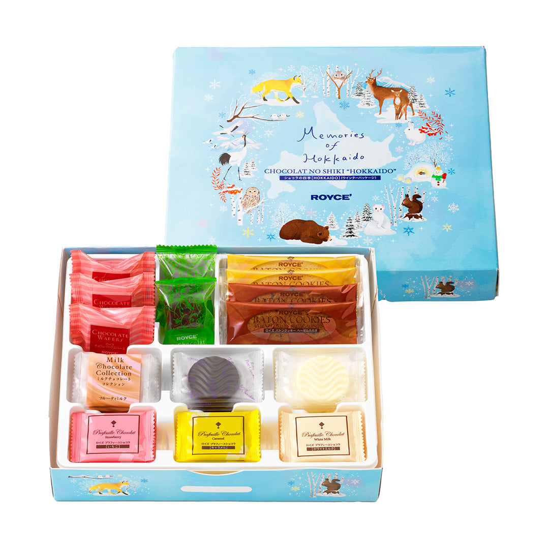 Image shows on upper middle right a blue box with illustrations of a fox, deer, a crane, owls, a bear, squirrels, a snowman, a cat, a rabbit, and snow-covered trees and landscapes. Text in the middle says Memories of Hokkaido. Chocolat No Shiki "Hokkaido". ROYCE'. Lower middle left is an open box with individually-wrapped confections in different shapes and colors. Background is in white.