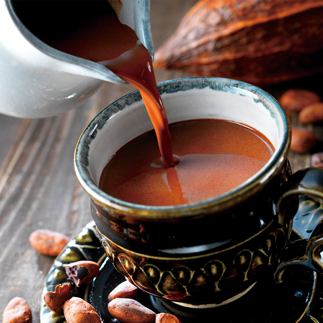 Image shows a cup with chocolate drink. Accents include loose cacao beans.