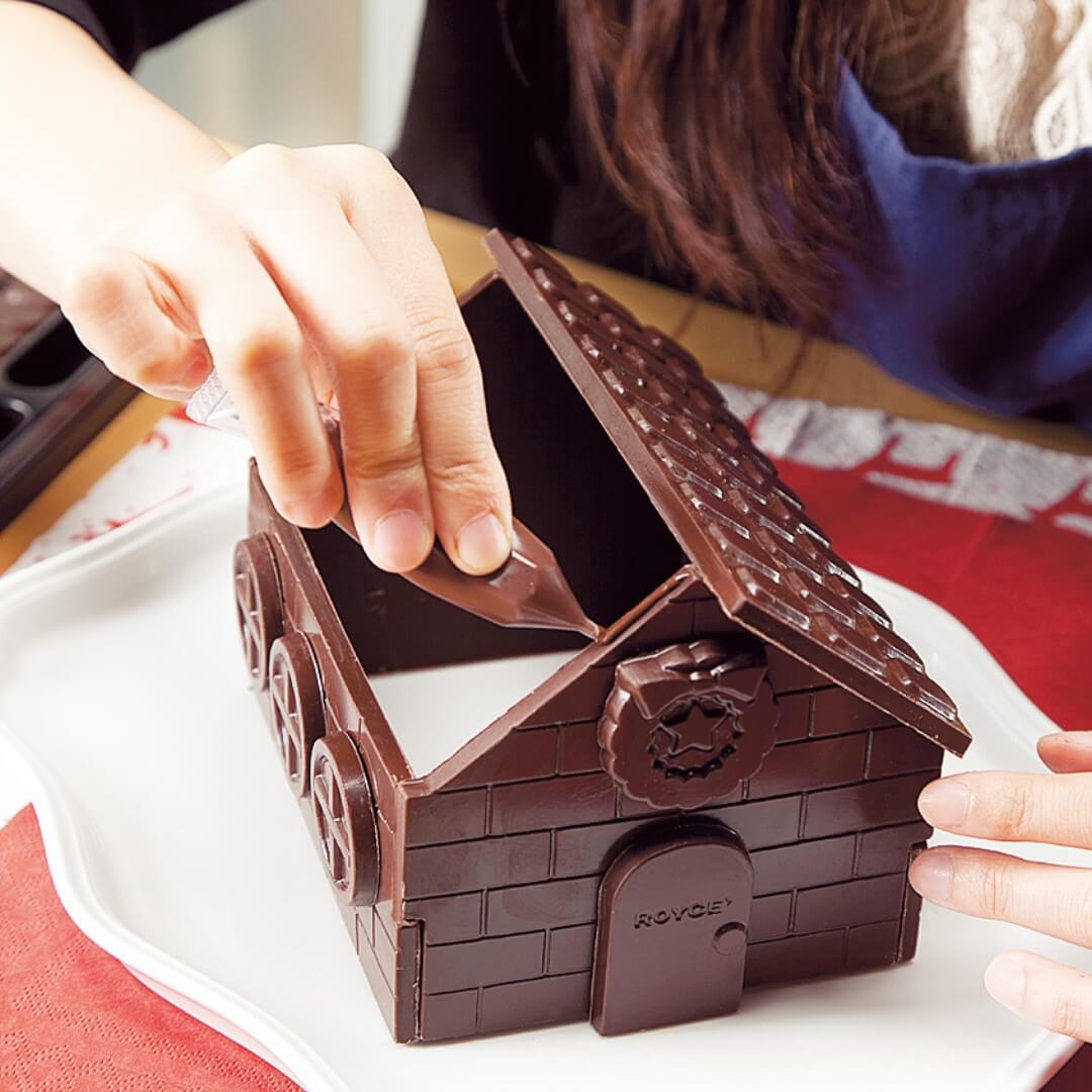 Chocolate No I-E - Image shows a person assembling a brown chocolate house.