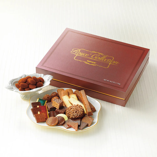 ROYCE’ Collection Brown gift box with a dish of cocoa-dusted almonds and a plate of assorted chocolates and cookies on a light surface.