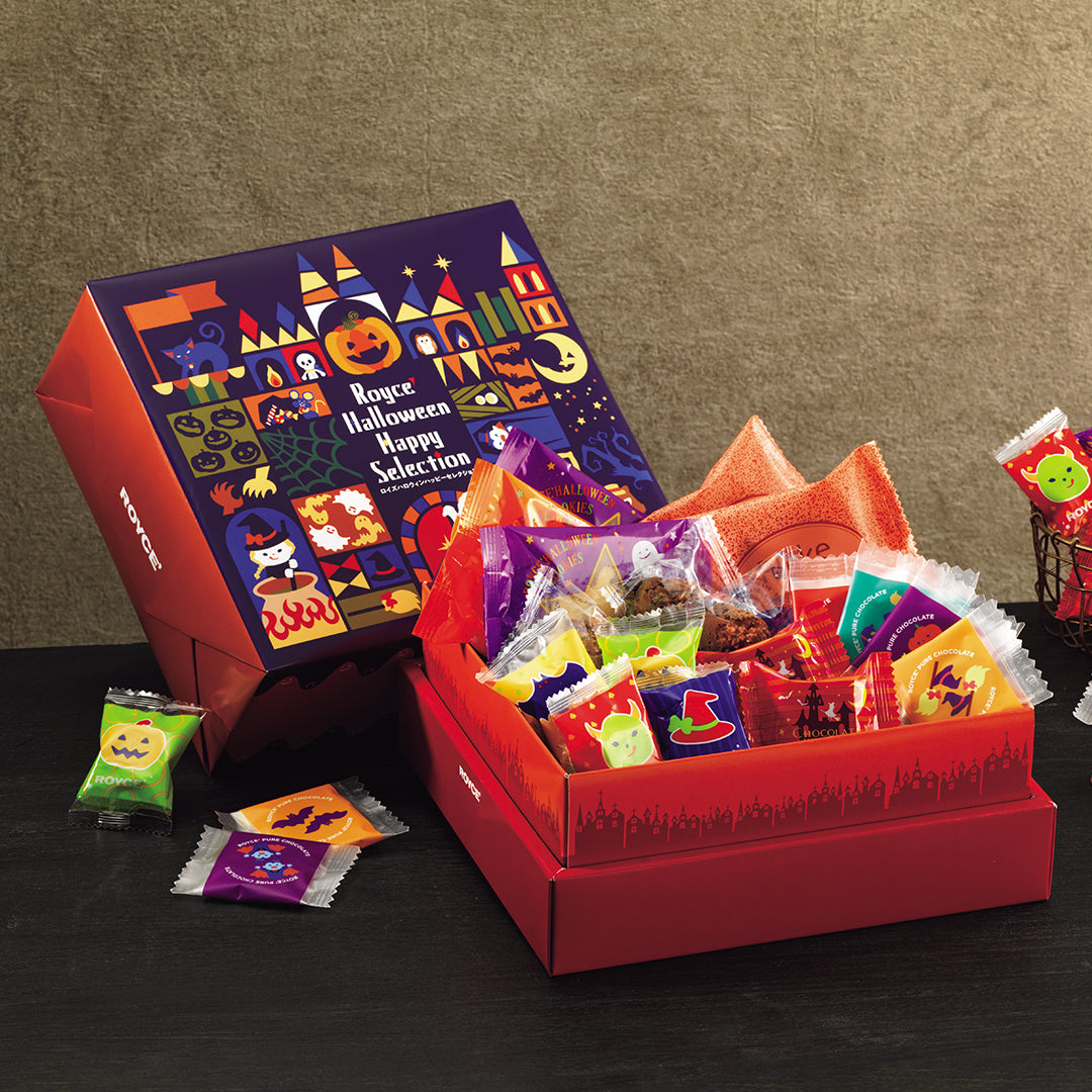 ROYCE' Halloween Happy Selection - A Halloween-themed gift set from ROYCE' featuring a large illustrated box, an open red box filled with assorted packaged confections, and several loose chocolates scattered on a dark tabletop against a beige wall.