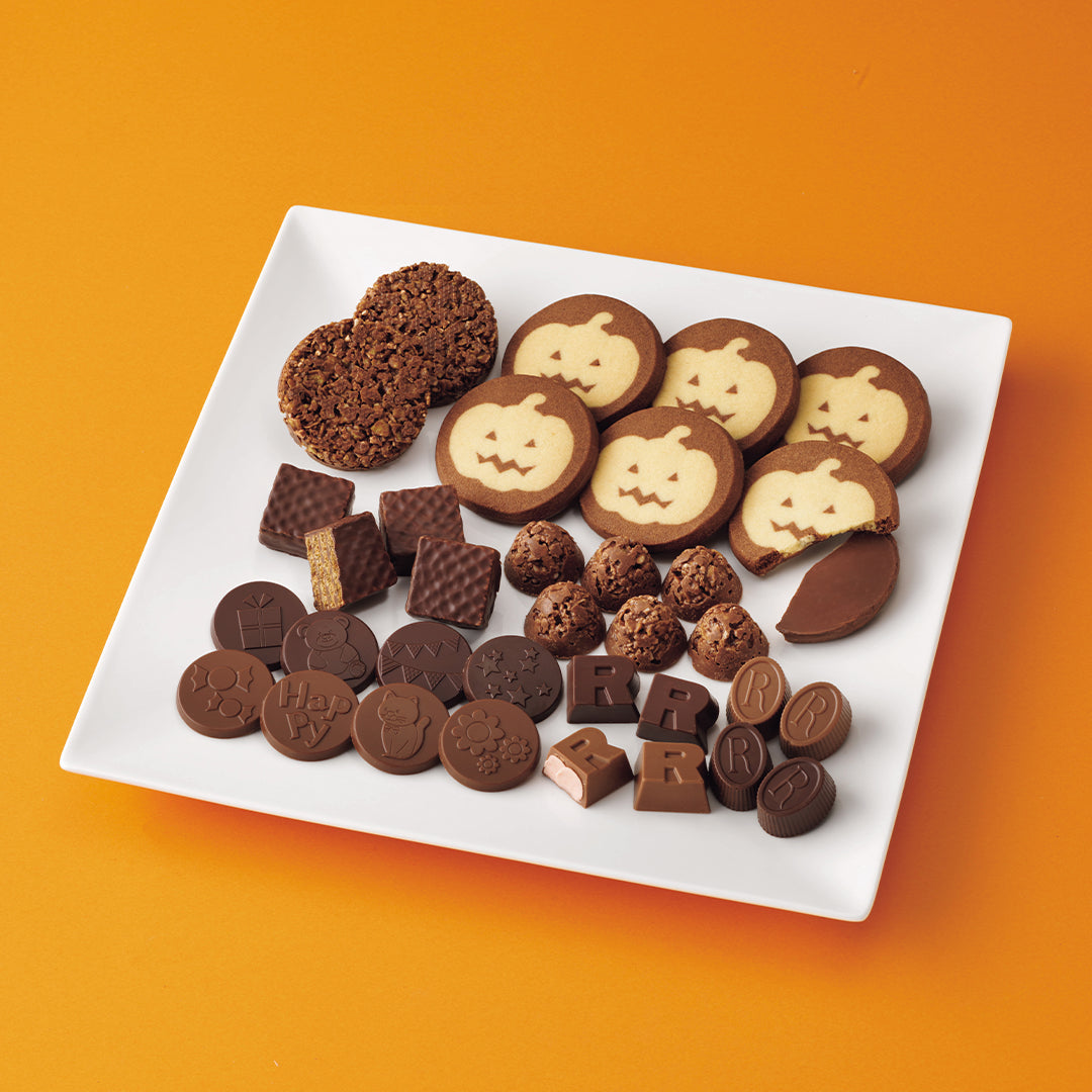 ROYCE' Halloween Happy Selection - An assortment of Halloween-themed chocolate treats and cookies arranged on a white square plate against a bright orange background. The treats include pumpkin-shaped cookies, chocolate bark, chocolate squares, and round chocolate pieces with Halloween motifs.