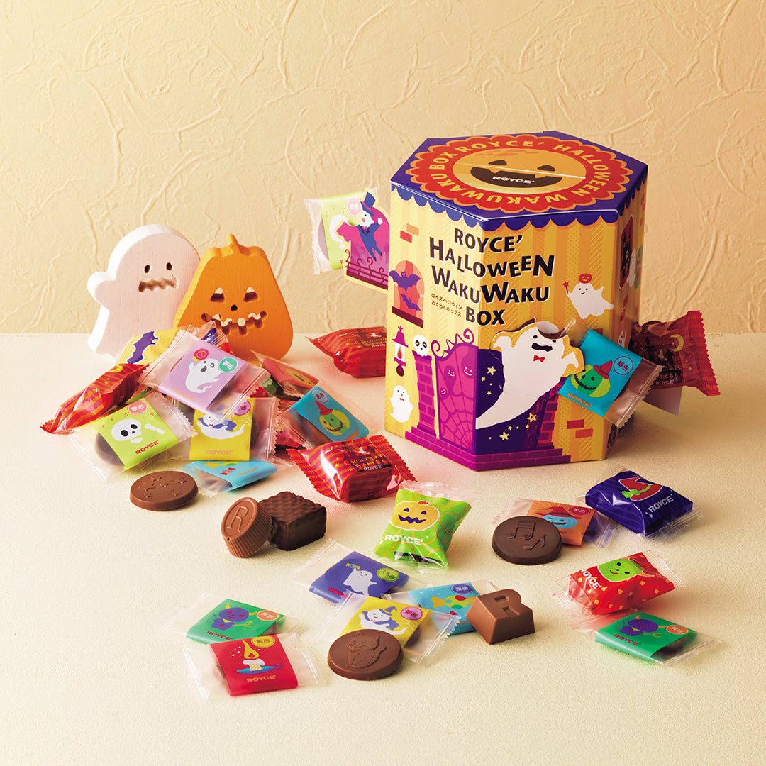 ROYCE' Halloween Wakuwaku Box - A colorful 'ROYCE' Halloween WakuWaku Box' filled with assorted Halloween-themed chocolates and treats, displayed on a cream-colored surface against a textured beige wall.