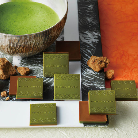 ROYCE' Kyoto Kokutoh & Uji Matcha Chocolate - Image shows chocolate squares in brown and green with the words ROYCE' Kyoto etched on them. Accents include a marbled plate, a cup with green tea, and a paper-like surface in white and orange.