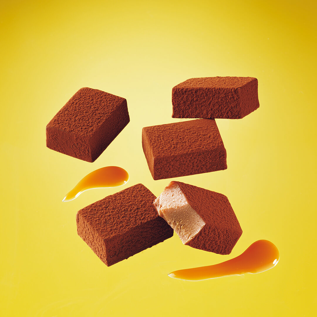 ROYCE' Chocolate - Nama Chocolate "Caramel Milk" - Image shows brown chocolate blocks with some caramel sauce. Background is in yellow.