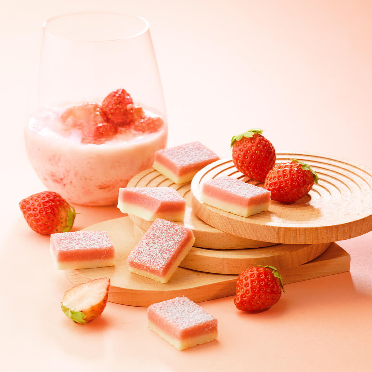 ROYCE' Chocolate - Nama Chocolate "Strawberry Milk" - Image shows pink and white chocolate blocks on wooden plates. Accents include strawberries and a glass of milk with strawberry. Background is in pink.