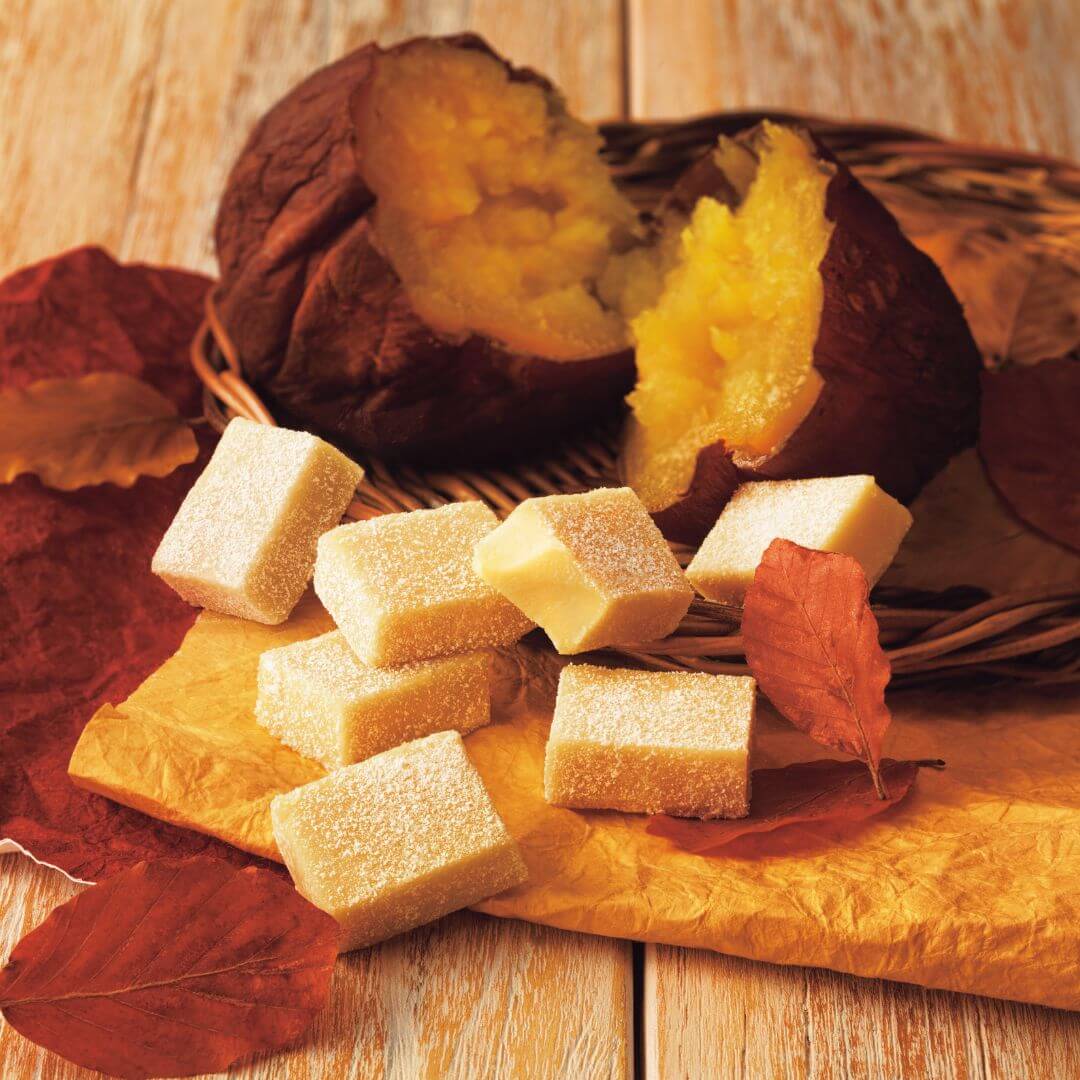 Nama Chocolate Roasted Sweet Potato displayed with open roasted sweet potatoes and sweet potato candy, set among autumn leaves on a wooden surface.