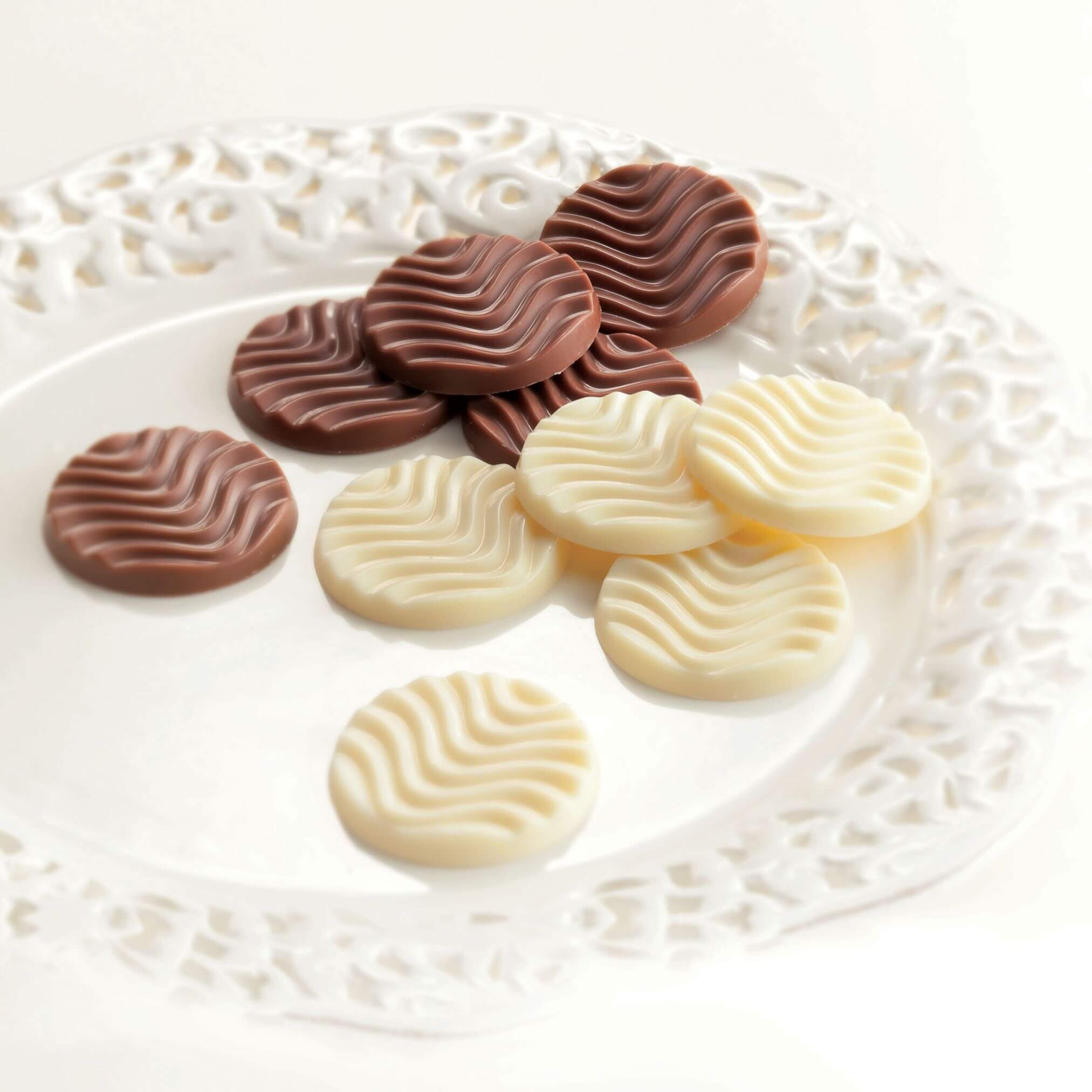 ROYCE' Chocolate - Pure Chocolate "Creamy Milk & White" - Image shows brown and white chocolate discs with a waved texture on a white plate with engravings. Background is in white color.
