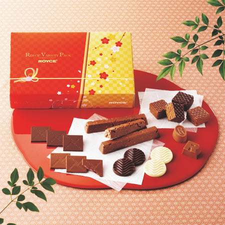 ROYCE' Variety Pack New Year - Image shows chocolates on a red plate with a printed box in red and yellow. Accents include leaves. Text says ROYCE' Variety Pack ROYCE'.