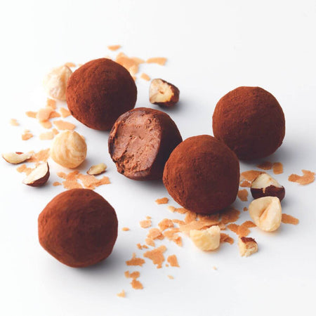 ROYCE' Chocolate - ROYCE’ Feuillantine Truffe “Gianduja” - Image shows brown chocolate truffles. Accents include loose baked flakes and bits of hazelnuts.