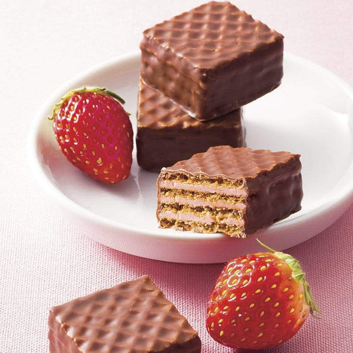 ROYCE' Chocolate - Chocolate Wafers "Strawberry Cream" - Image shows brown chocolate wafers with crisscrossed texture on a round white plate. Accents include red strawberries. Background is in a mix of pink and white colors.