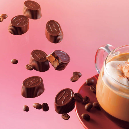 ROYCE' Chocolate - ROYCE' R Chocolat "Caffé Mocha" - Image shows oval-shaped brown chocolates engraved with the letter R. Accents include brown coffee beans and a cup of coffee on a plate. Background is in pink.