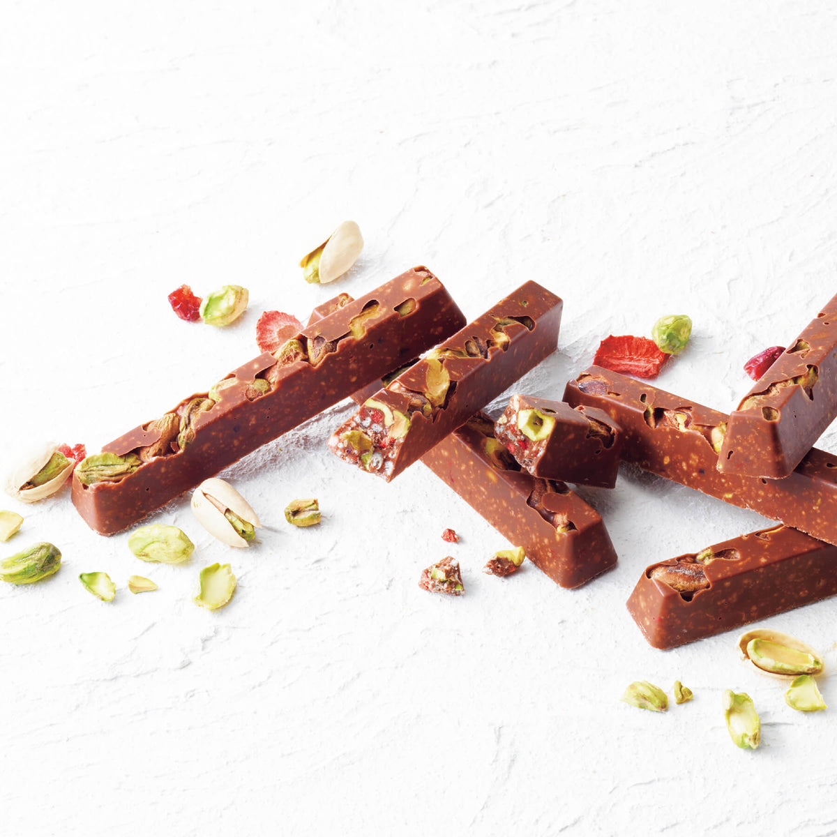 ROYCE' Chocolate - ROYCE' Bar Chocolate "Pistachio" - Image shows finger-shaped brown chocolate bars with pistachio nuts and berries inside. Accents include loose pistachio nuts and dried berries. Textured background is in white.