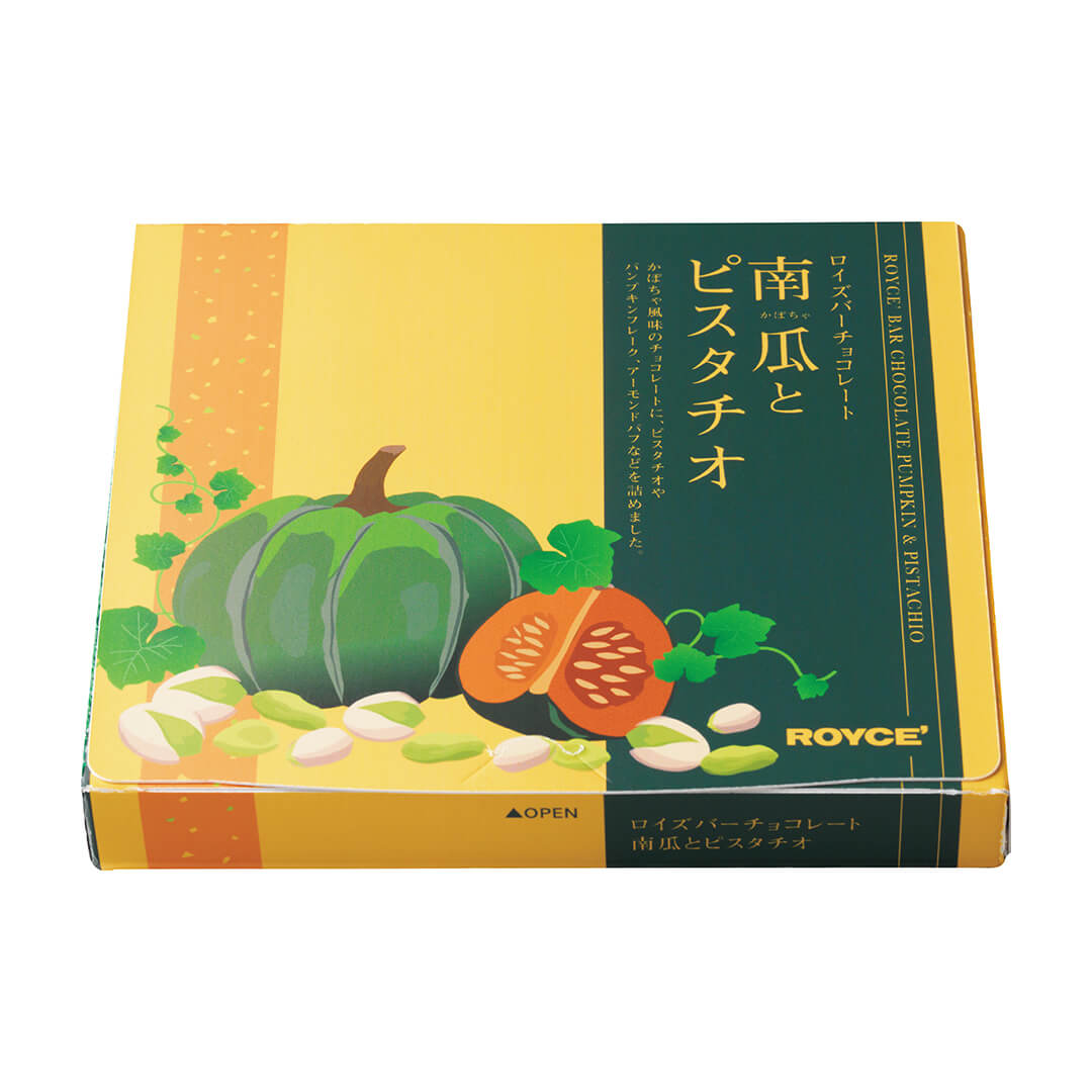Image shows a printed box in yellow, orange, and green, with illustrations of loose pistachio nuts in light yellow and green together with pumpkins and leaves in green and orange. Text on upper right from top to bottom says ROYCE' Bar Chocolate Pumpkin & Pistachio. ROYCE'. Green text on the bottom middle center of the box says Open with a green upward arrow on the left.