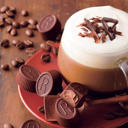 ROYCE' Chocolate - ROYCE' R Chocolat "Caffé Mocha" - Image shows oval-shaped brown chocolates engraved with letter R on a plate with wooden spoon and a cup of coffee. Background has brown wood and brown coffee beans.