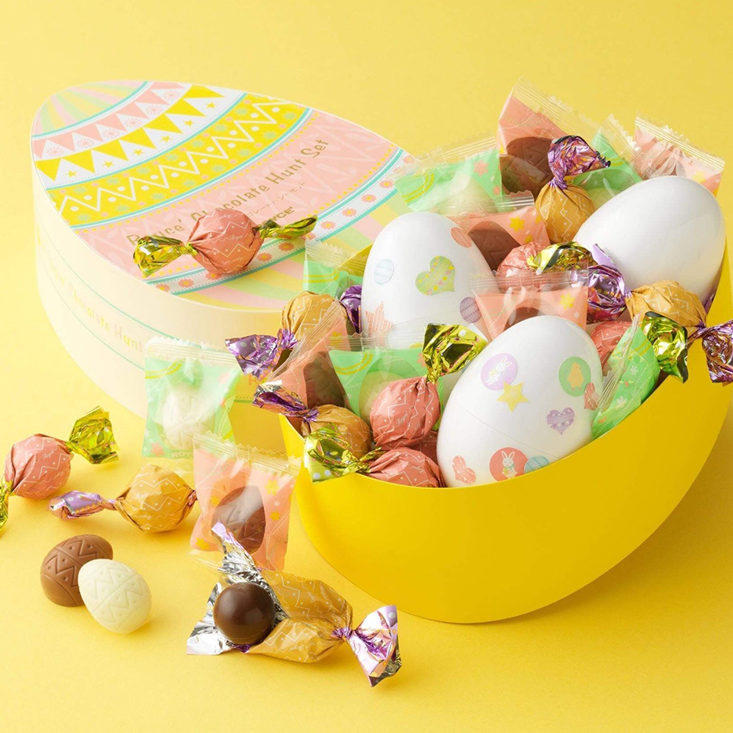 ROYCE' Chocolate - ROYCE' Chocolate Hunt Set - Image shows two egg-shaped boxes with a yellow background. Printed box on upper left has text saying ROYCE' Chocolate. Yellow box on right has printed plastic eggs and a variety of confections in different colors and sizes.