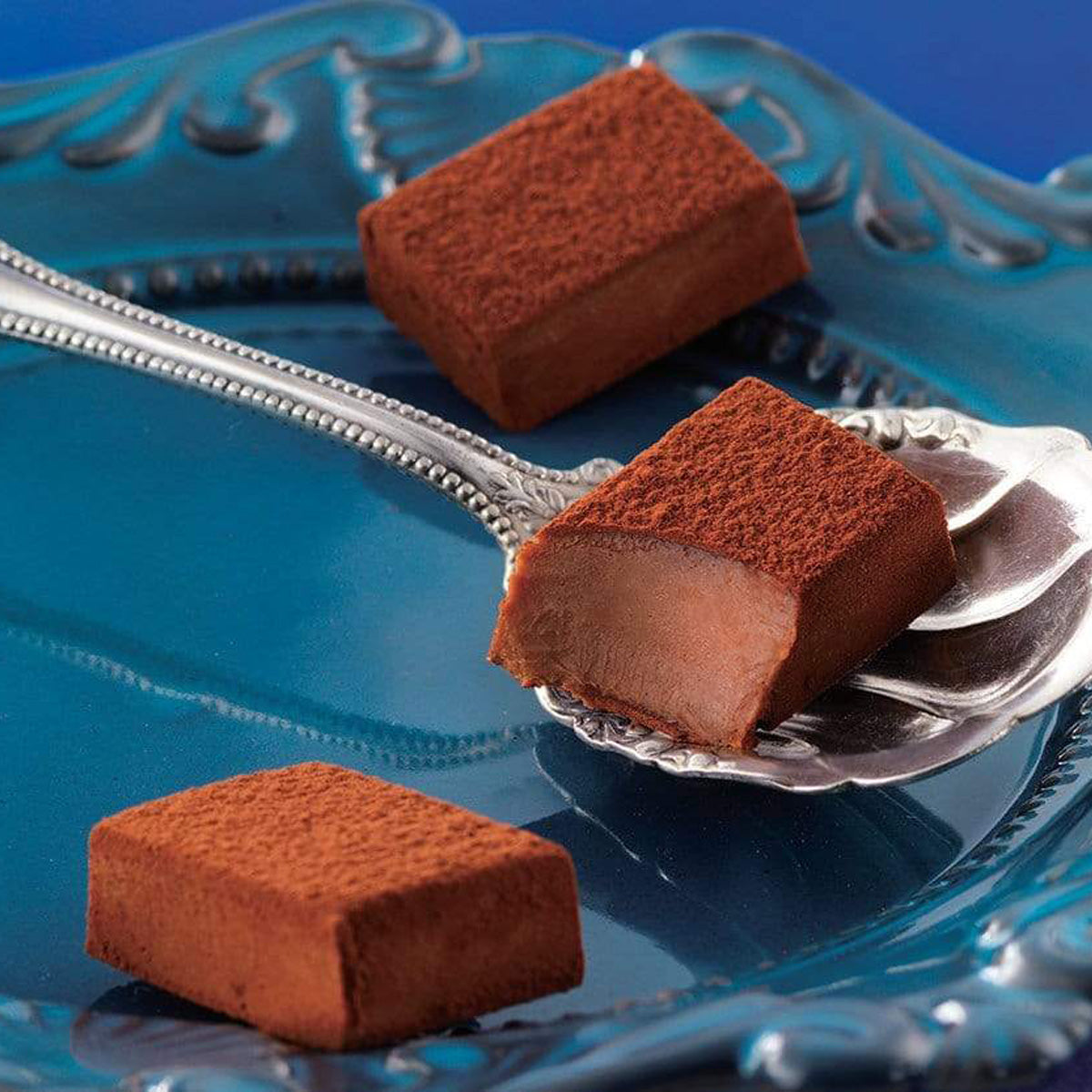ROYCE' Chocolate - Nama Chocolate "Au Lait" - Image shows brown blocks of chocolate on a blue plate with a silver spoon.