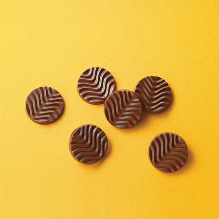 ROYCE' Chocolate - Pure Chocolate "Fruity Milk" - Image shows brown chocolate discs with a waved texture. Background is in color yellow.