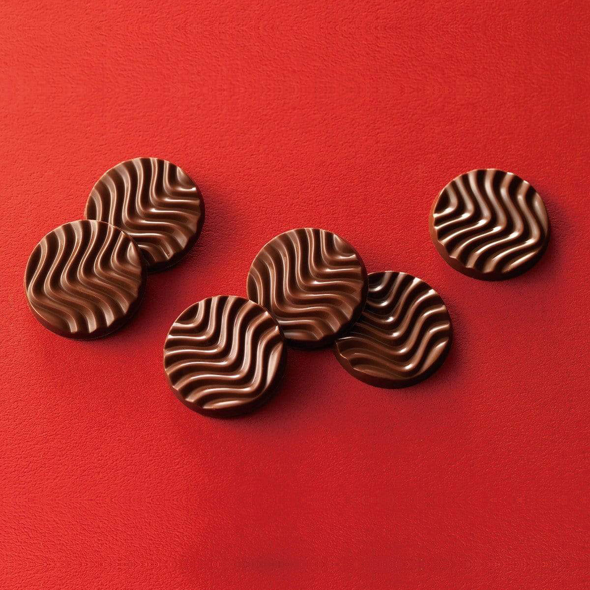 ROYCE' Chocolate - Pure Chocolate "Milk" - Image shows brown chocolate discs with a waved texture. Background and surface is in red color.