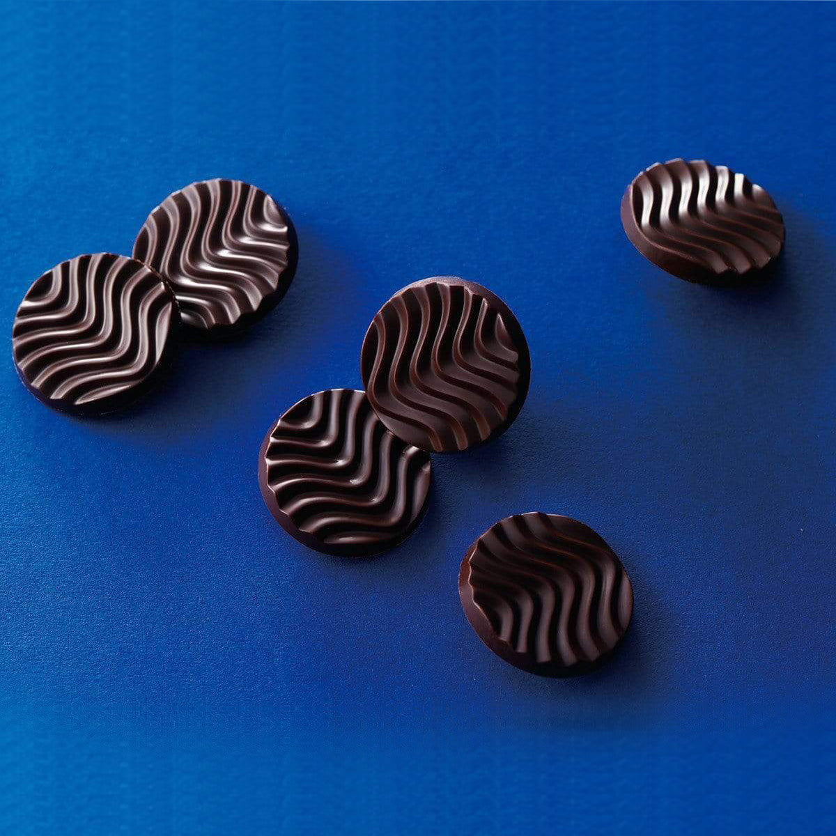 ROYCE' Chocolate - Pure Chocolate "Venezuela Bitter" - Image shows dark brown chocolate discs with waved texture. Background and surface is in blue color.