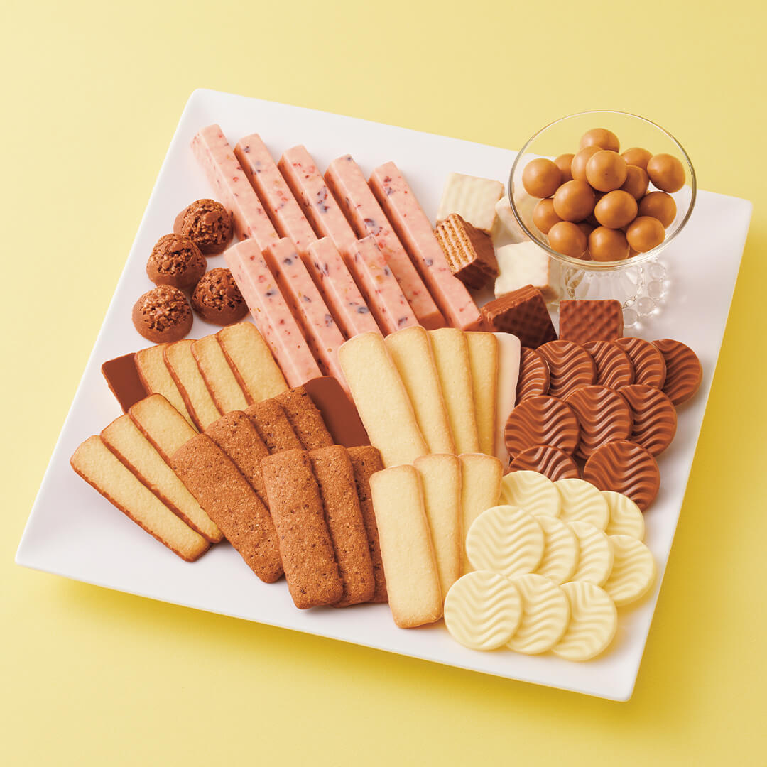 ROYCE' Chocolate - ROYCE' Collection "Sweet Yellow" - Image shows a white square-shaped plate filled with various confections in different shapes and sizes in the colors brown, pink, white, and yellow. Background is in color yellow.