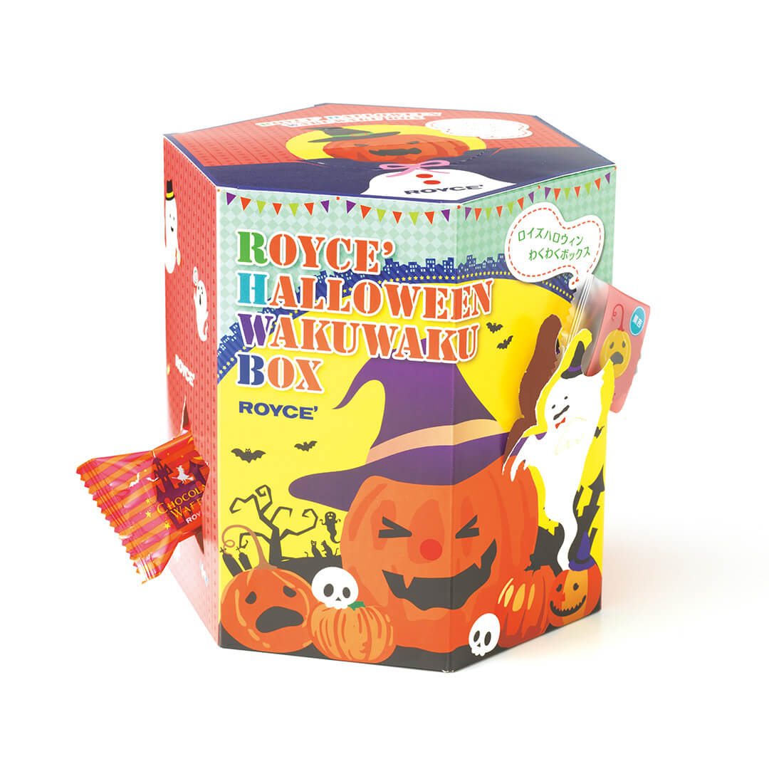 Image shows a hexagon-shaped printed box in the colors of red, blue, green, yellow, orange, and white. Text on the box (from top to front middle) says ROYCE'. ROYCE' Halloween Wakuwaku Box. ROYCE'. White text on the side of the box says ROYCE'. Seen in the picture are illustrations of ghosts, pumpkins with facial expressions, bats, trees, towers, skulls, tombstones, and cats. Sides also show wrapped chocolates in the colors of red and yellow. Background is in white. 