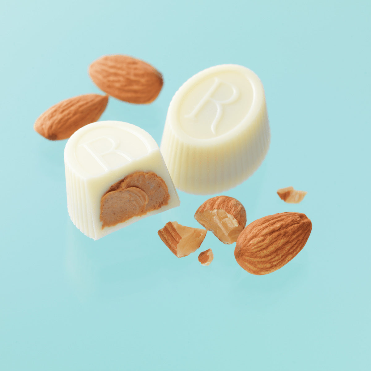 ROYCE' Chocolate - ROYCE' R Chocolat "White Gianduja" - Image shows white chocolate cups filled with a brown cream. Accents are loose almonds. Background is in light blue color.