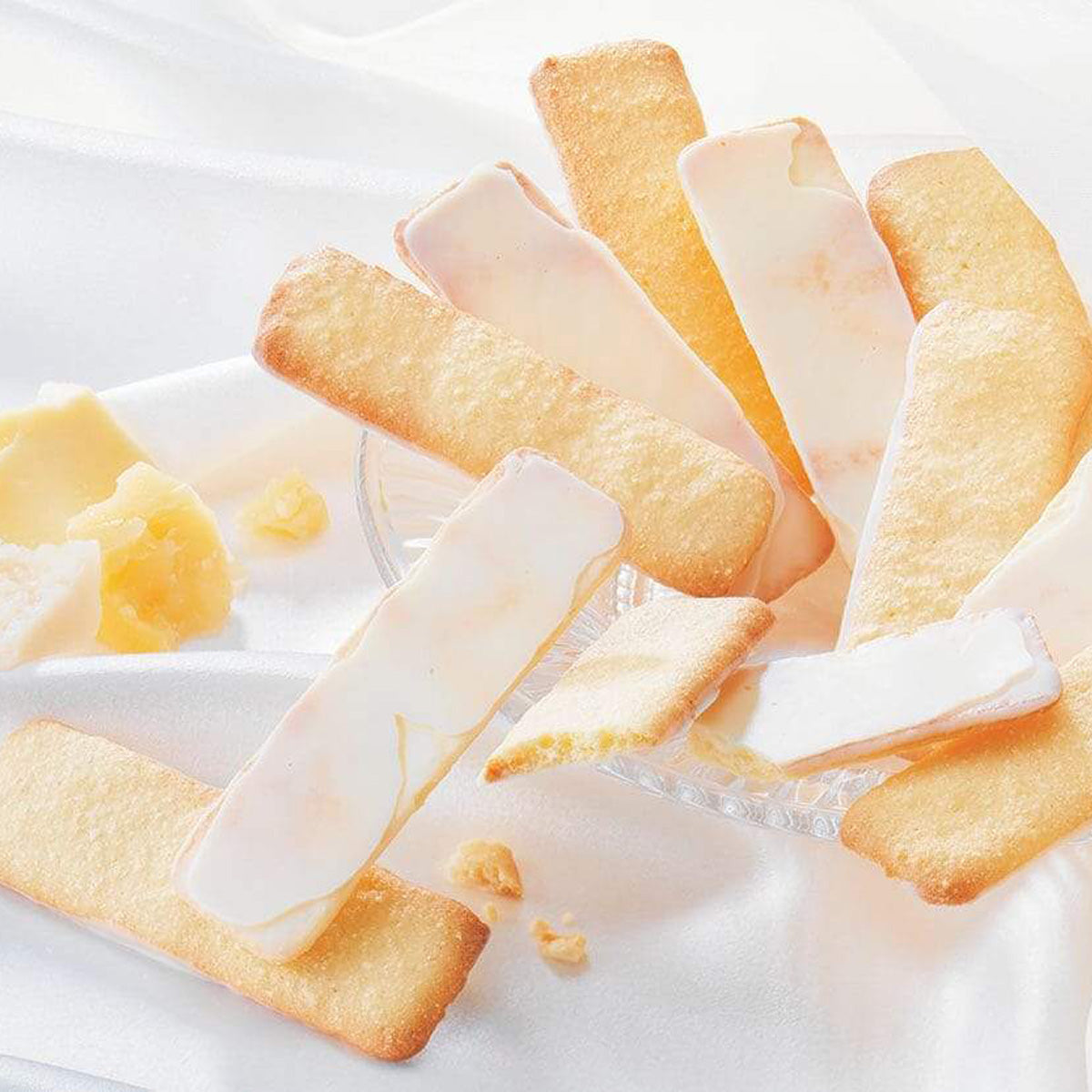 ROYCE' Chocolate - Baton Cookies "Fromage (25 Pcs)" -  Image shows golden cookies coated with white chocolate on crystal bowl. Accents include blocks of cheese. Background is in white. 