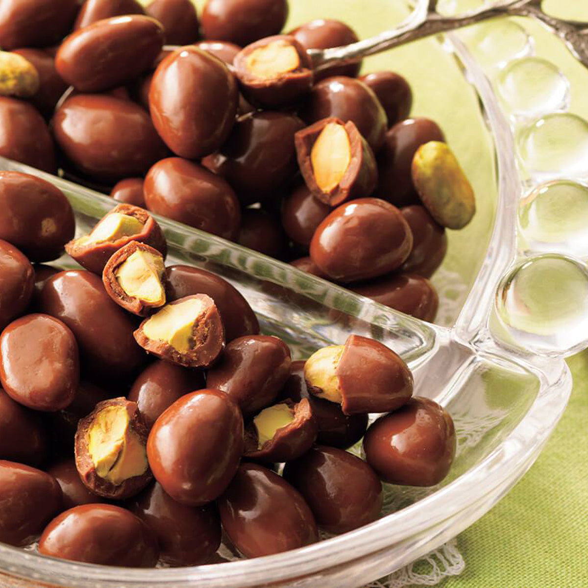 ROYCE' Chocolate - Pistachio Chocolate - Image shows a clear bowl filled with brown chocolate-coated pistachios. 