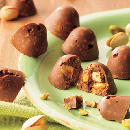 ROYCE' Chocolate - Pistachio Crunch Chocolate - Image shows a green plate filled with brown chocolate creations with pistachios. 