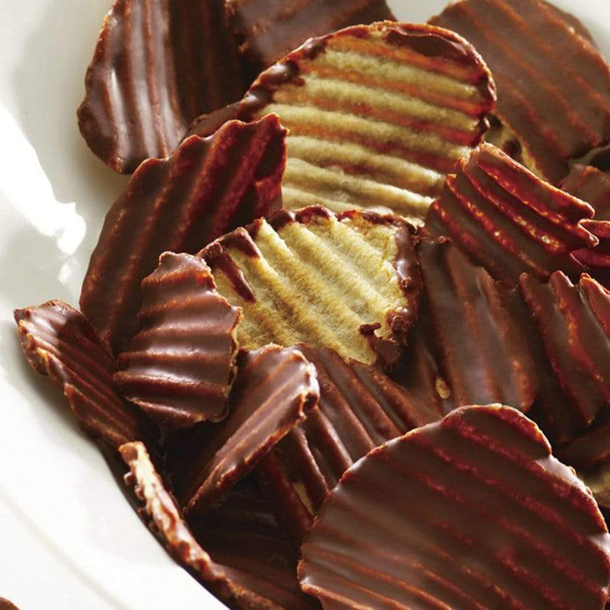 ROYCE' Chocolate - Potatochip Chocolate "Original" - Image shows brown chocolate-covered potato chips with a ridged texture, as placed on a white plate.