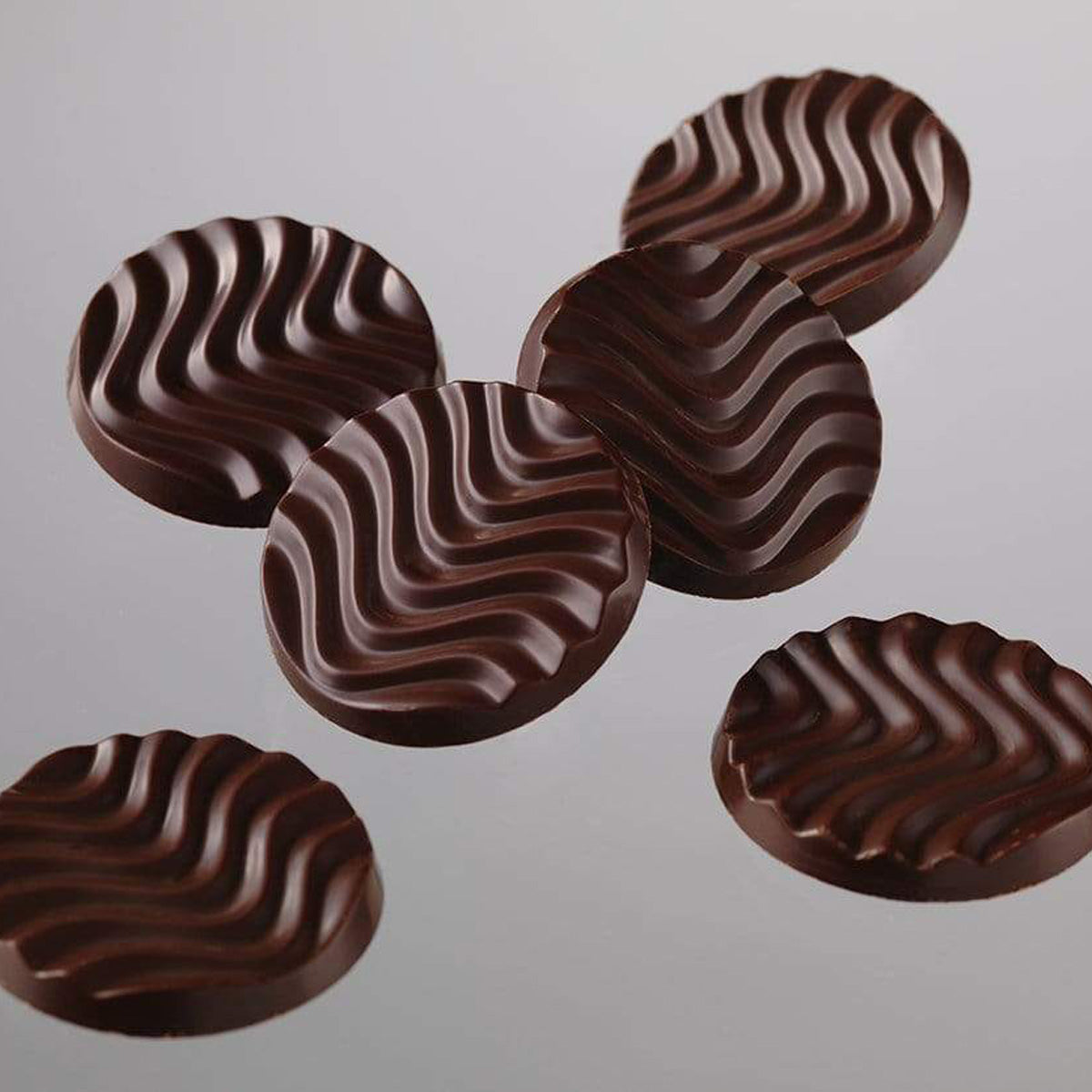 ROYCE' Chocolate - Pure Chocolate "Mild Bitter & Extra Bitter" - Image shows a black chocolate discs with a waved texture. Background is in color gray.