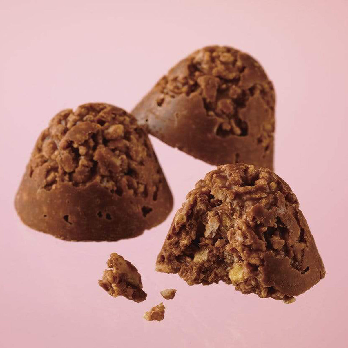 ROYCE' Chocolate - Potechi Crunch Chocolate - Image shows brown chocolate creations filled with crumbled potato chips, cornflakes, and cookie bits inside. Background is in pink color.