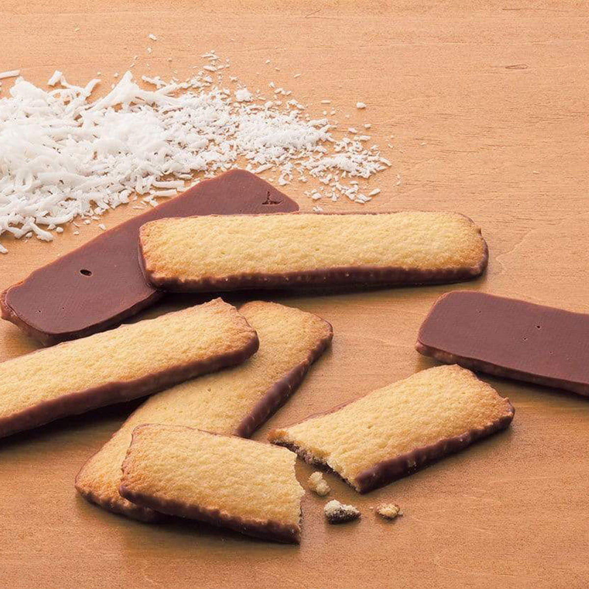 ROYCE' Chocolate - Baton Cookies "Coconut" - Image shows golden cookies with brown chocolate coating and white coconut shavings on a brown-colored surface.