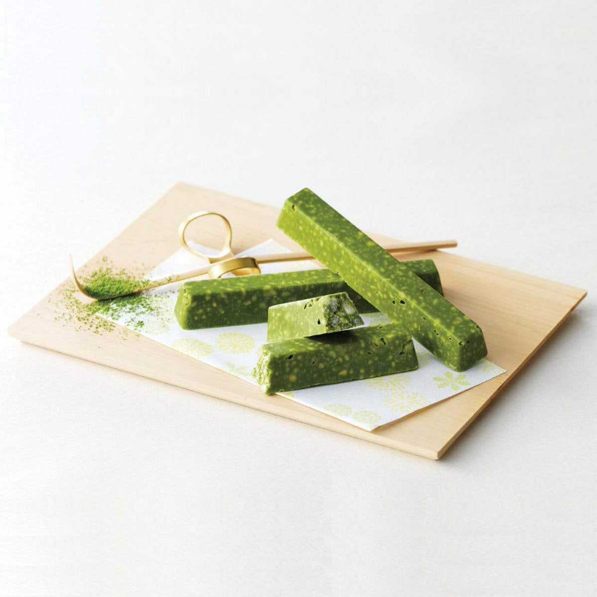 ROYCE' Chocolate - Matcha Bar Chocolate - Image shows green chocolate bars on a white printed paper with accents of green tea powder, a wooden stick, and a brown wooden platform. Background is in white.