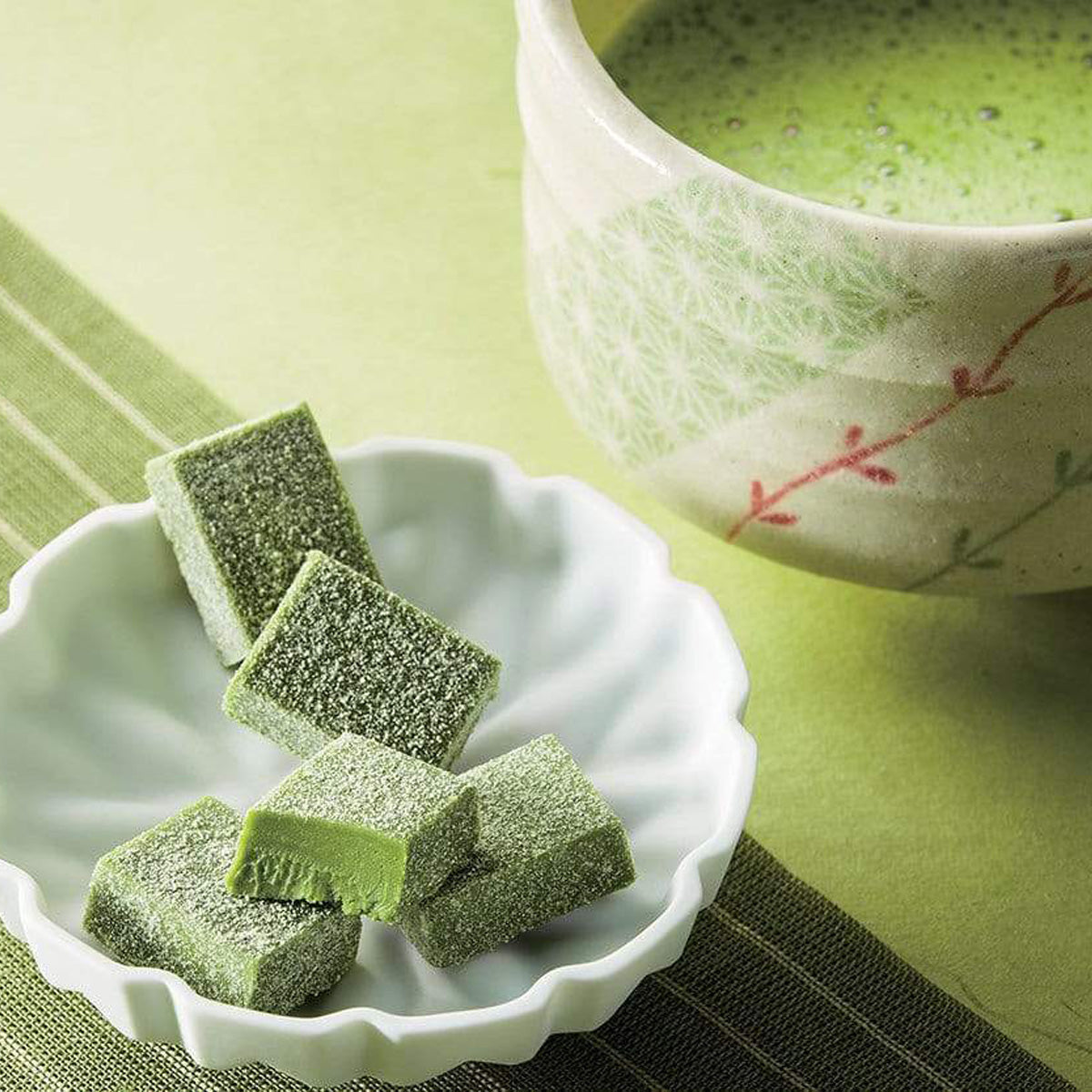ROYCE' Chocolate - Nama Chocolate "Matcha" - Image shows green blocks of chocolates on a flower-shaped plate. Accents include a green placemat and a tea cup with floral prints, as filled with green tea.
